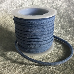 May include: A spool of navy blue suede leather cord. The cord is rolled neatly on a white and gray plastic spool. The suede has a textured appearance. The cord is a continuous loop, with a portion unwound.