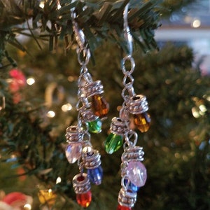 May include: A pair of silver dangle earrings with colorful glass beads. The beads are shaped like light bulbs and are arranged in a cascading pattern. The earrings are a fun and festive way to add a touch of holiday cheer to any outfit.