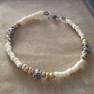 May include: A white and yellow beaded bracelet with silver skull charms.