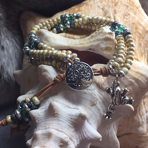 May include: A multi-strand bracelet with brown leather cord, silver beads, and green and cream colored glass beads. The bracelet has a silver charm of a tree of life and a silver frog charm.