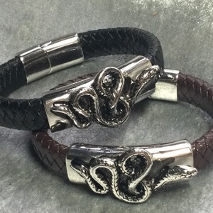 May include: Two braided leather bracelets with silver snake head clasps. One bracelet is black and the other is brown.