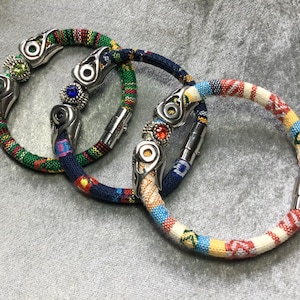 May include: Three colorful woven bracelets with silver metal accents and decorative stones. The bracelets have a magnetic clasp.