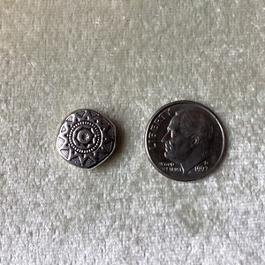 May include: A silver-toned metal charm with a geometric starburst design. The charm is about the size of a dime.
