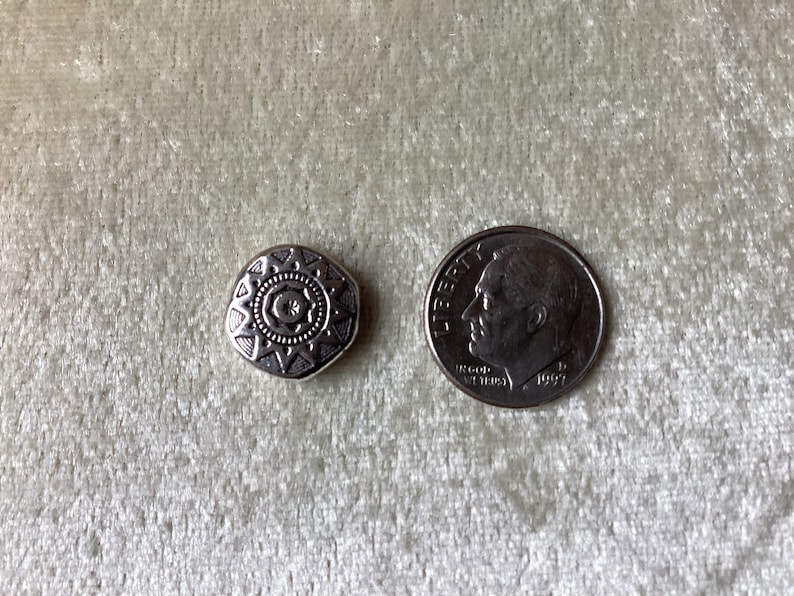 May include: A silver-toned metal charm with a geometric starburst design. The charm is about the size of a dime.