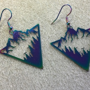 May include: A pair of iridescent earrings shaped like a triangle with a mountain and tree silhouette design.