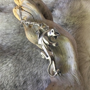May include: A silver-colored metal keychain featuring a detailed panther design. The panther is depicted in a dynamic pose, with its claws extended. The keychain is attached to a chain and ring. The background is a piece of driftwood.