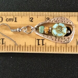 May include: Silver teardrop-shaped earring with a turquoise flower charm and brown and turquoise beads. The earring is approximately 2 cm long and has a silver hook.