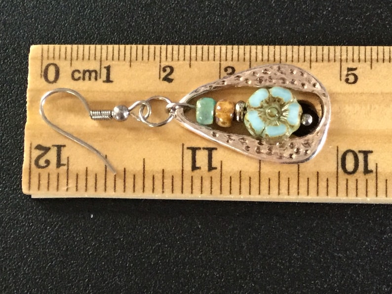 May include: Silver teardrop-shaped earring with a turquoise flower charm and brown and turquoise beads. The earring is approximately 2 cm long and has a silver hook.