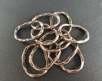 May include: A group of eight copper-colored metal rings, each with a hammered texture, are piled together on a dark gray surface.