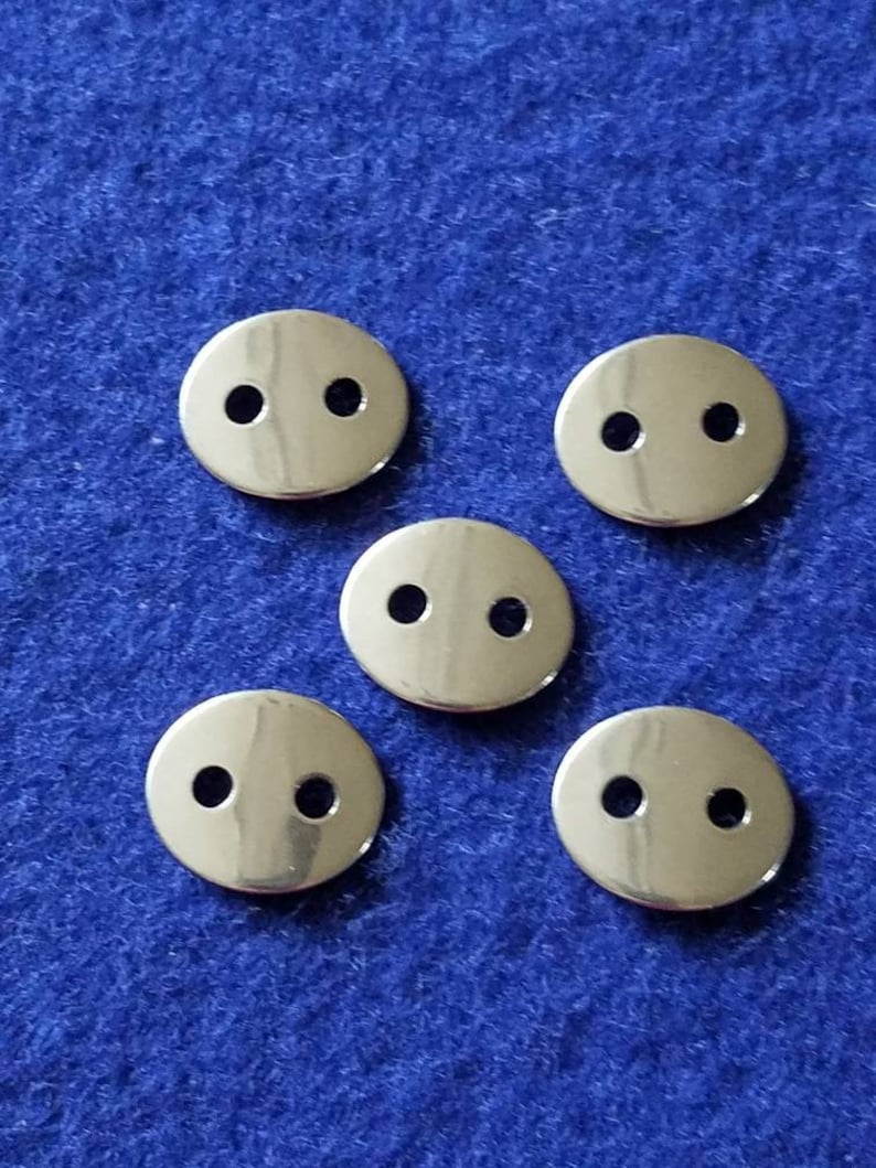 May include: Five silver metal buttons with two holes each. The buttons are round and have a shiny finish.