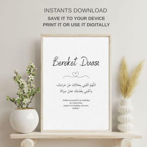 以下が含まれることがあります： エレガントな筆記体で「Bereket Duası」と書かれた額入りのプリント。プリントにはアラビア語のテキストと英語の翻訳が含まれており、ハートのシンボルが付いています。フレームは、装飾的な花瓶と植物が置かれた木製の棚に飾られています。