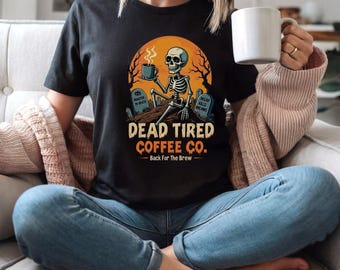 May include: Black t-shirt with a graphic featuring a skeleton drinking coffee, set against an orange sunset backdrop. The text reads "DEAD TIRED COFFEE CO." with "Back For The Brew" below. The design includes tombstones and trees.