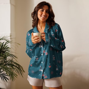 May include: A long-sleeved button-down pajama shirt in dark teal featuring a repeating pattern of pink and white science-themed icons including beakers, flasks, test tubes, and atomic symbols, paired with light gray shorts.