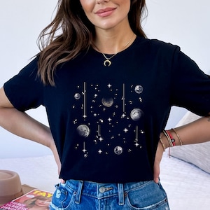 May include: Black t-shirt featuring a celestial design. The graphic includes planets, stars, and lines, all in white. The planets have a textured appearance. The shirt is a crew neck and has short sleeves.