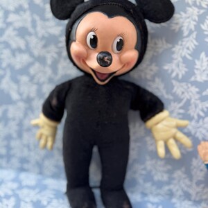 May include: Vintage Mickey Mouse doll in a black jumpsuit with a smiling face, large black ears, and cream-colored gloves. The doll's face is tan with black eyes and a black nose. A classic Disney collectible.