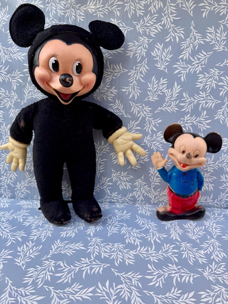May include: Two vintage Mickey Mouse figurines. One is a plush doll in a black outfit with a smiling face and cream-colored hands. The other is a small plastic figurine of Mickey Mouse in a blue shirt and red pants, waving.