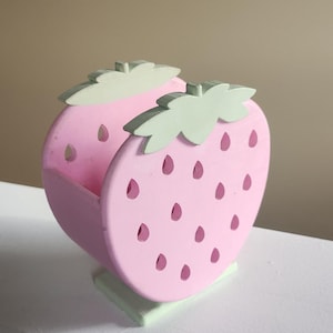 Peut inclure: Un plat en bois en forme de fraise rose et verte. Le plat a un motif d&eacute;coup&eacute; en forme de fraise avec des graines et des feuilles.