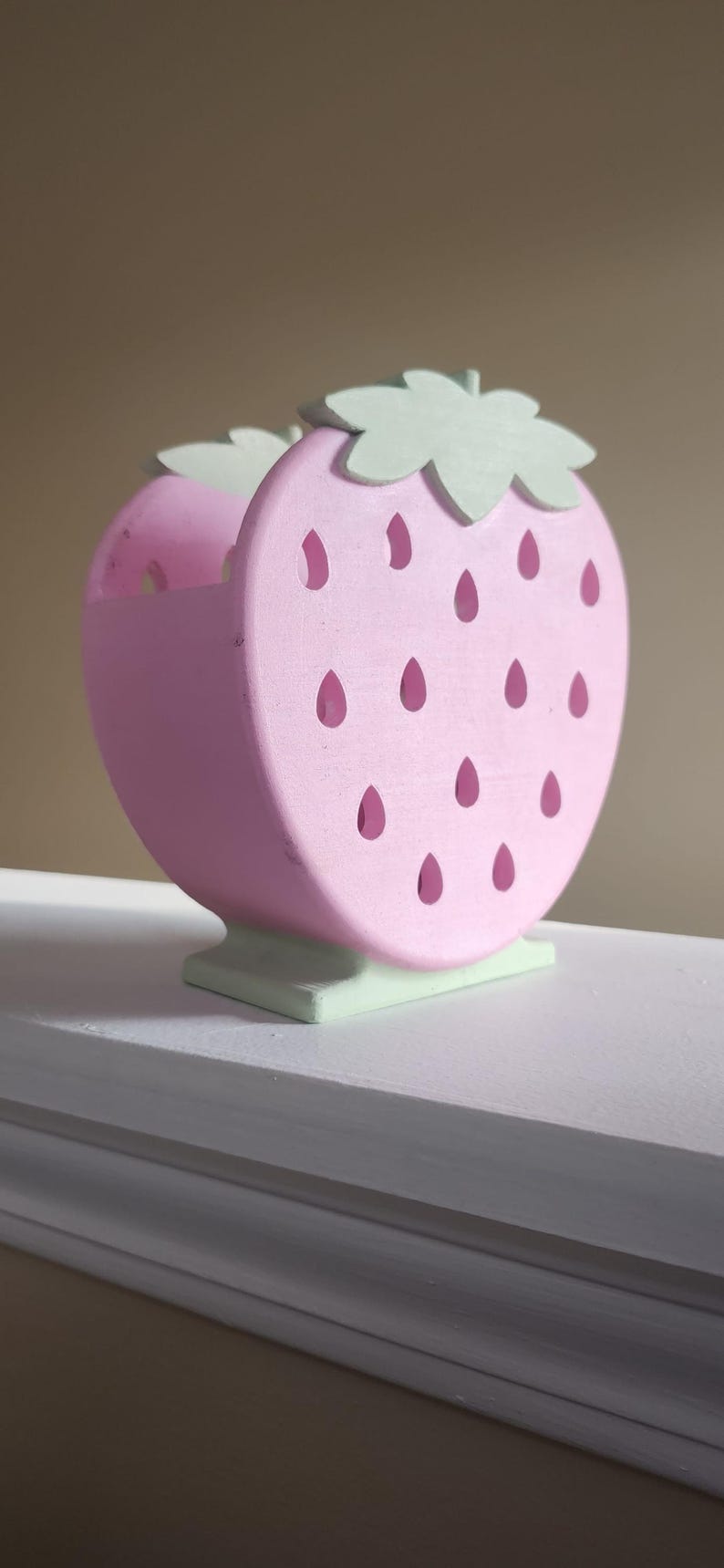 Peut inclure: Un organisateur en bois en forme de fraise rose et verte avec des d&eacute;tails d&eacute;coup&eacute;s. L'organisateur a une base plate et est parfait pour ranger de petits objets.