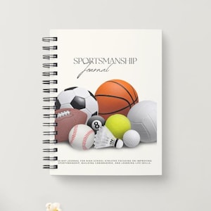 Puede incluir: Un cuaderno blanco de espiral con el título "Sportsmanship Journal" impreso en negro. La portada presenta una ilustración colorida de varios balones deportivos, incluyendo un balón de baloncesto, un balón de fútbol, un balón de béisbol y un balón de voleibol.