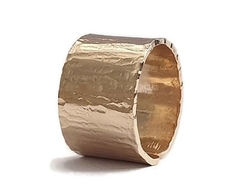 May include: A gold ring with a textured, hammered finish. The ring is wide and has a rounded shape.