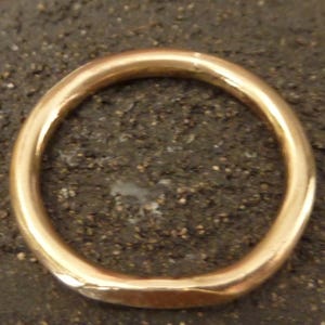 May include: A gold-colored ring with a smooth, rounded design. The ring is circular and appears to be made of metal. The ring is set against a dark, textured background, highlighting its polished surface. This piece of jewelry is suitable for everyday wear.