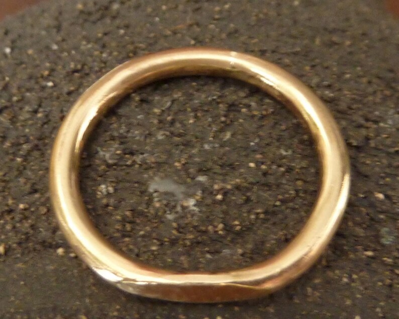 May include: A gold-colored ring with a smooth, rounded design. The ring is circular and appears to be made of metal. The ring is set against a dark, textured background, highlighting its polished surface. This piece of jewelry is suitable for everyday wear.