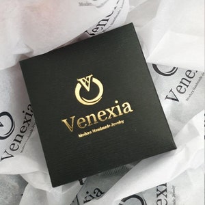 May include: A black square box with a gold logo that says "Venexia Modern Handmade Jewelry".