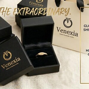 May include: Black jewelry boxes with gold lettering and a ring displayed in an open box. The text "UNBOX THE EXTRAORDINARY" is visible. A shopping bag and a graphic with text about gold vermeil are also in the image. The brand name is Venexia.