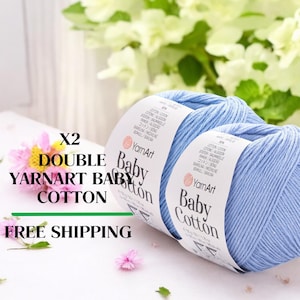May include: Two light blue YarnArt Baby Cotton yarn skeins. The image includes text that reads "X2 DOUBLE YARNART BABY COTTON". The yarn is displayed with flowers in the background.