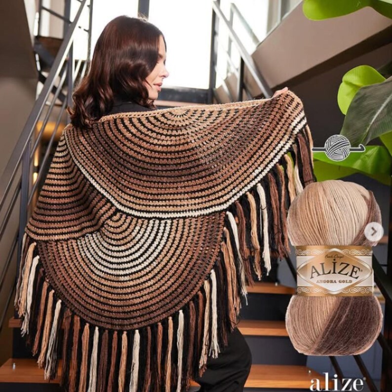 May include: A brown and cream-colored crocheted shawl with fringe. The shawl is circular with concentric rows of color. A ball of Alize Angora Gold yarn is in the image, with a label that reads "Alize Angora Gold".