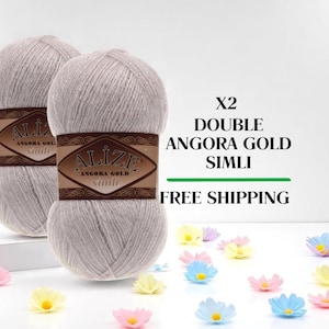 May include: Two skeins of light gray Angora Gold Simli yarn with brown labels. The image includes the text "X2 DOUBLE ANGORA GOLD SIMLI". Decorative colorful flower accents are scattered around the yarn.