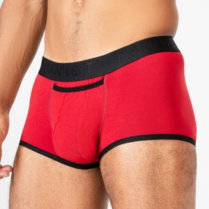 May include: Red boxer briefs with black trim and a black waistband. The waistband features the text "MAN'S SET". The briefs have a pouch in the front and are made of a soft material.