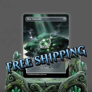 May include: A fantasy art card titled "Mox Emerald" featuring a green gemstone pendant with a silver chain resting on a green pillow. The card is displayed on a stone pedestal with green crystal accents.