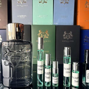 Pu&ograve; includere: Un flacone di profumo in vetro trasparente con tappo argentato e un'emblema di cavallo, circondato da fiale campione e scatole. Le scatole sono di vari colori, tra cui blu, verde e arancione. Le fiale sono etichettate con "SAMPLE".