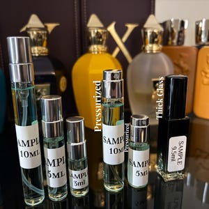 Pu&ograve; includere: Un assortimento di campioni di profumo in flaconi di vetro trasparente con tappi argentati. I campioni sono etichettati con dimensioni come 10 ml, 5 ml e 3 ml. Diverse bottiglie di profumo di dimensioni standard in vari colori sono visibili sullo sfondo.