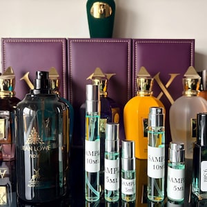 May include: A collection of perfume bottles and sample vials. The bottles have different shapes, colours, and sizes, with gold-coloured caps. The samples are labelled with sizes like 10ml, 5ml, and 3ml. The image includes the text "JEAN LOWE noir".
