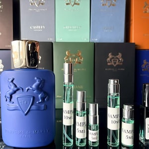 May include: A collection of fragrances, including a large blue bottle with a gold cap and a horse emblem, and several sample-sized spray bottles. The background features various boxes with embossed logos and text.