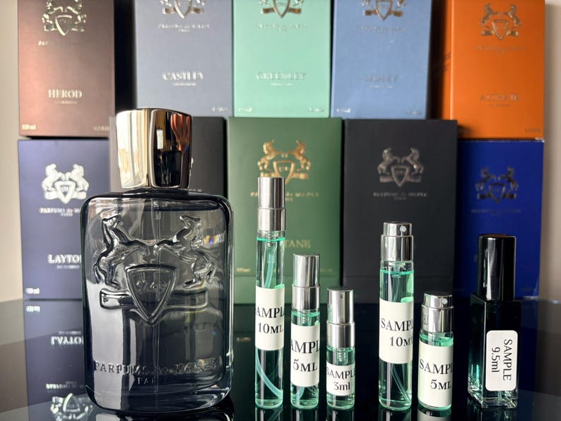 Pu&ograve; includere: Un flacone di profumo in vetro trasparente con tappo argentato e un'emblema di cavallo, circondato da fiale campione e scatole. Le scatole sono di vari colori, tra cui blu, verde e arancione. Le fiale sono etichettate con "SAMPLE".