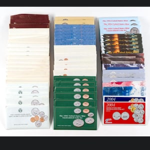 May include: A collection of United States Mint uncirculated coin sets arranged in three vertical stacks. The sets feature various colored envelopes and packaging, including text identifying them as United States Mint Uncirculated Coin Sets.