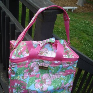 K&ouml;nnte beinhalten: Eine Tragetasche mit rosa-blauem Blumenmuster und passendem Schulterriemen. Die Tasche hat einen Rei&szlig;verschluss oben, eine Vordertasche und ein goldfarbenes Logo. Das Blumenmuster umfasst rosa Bl&uuml;ten und gr&uuml;ne Bl&auml;tter auf hellblauem Hintergrund.