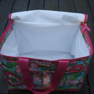 K&ouml;nnte beinhalten: Eine rechteckige Tragetasche mit einem Blumenmuster in Rosa, Gr&uuml;n und Blau. Die Tasche hat ein wei&szlig;es Innenfutter und rosa Griffe. Die Tasche ist offen und gibt den Blick ins Innere frei. Die Au&szlig;enseite hat ein Blumenmuster.