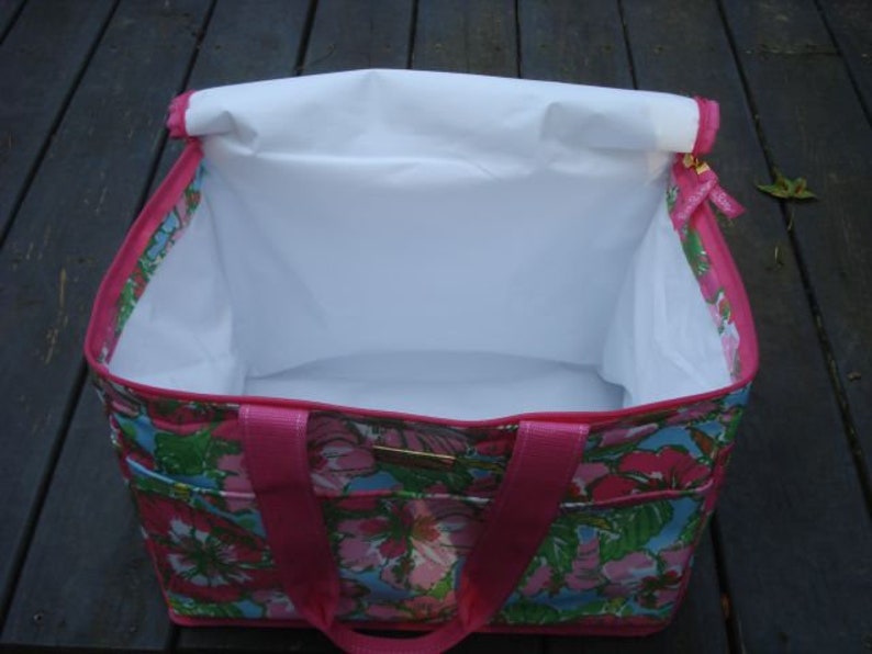 K&ouml;nnte beinhalten: Eine rechteckige Tragetasche mit einem Blumenmuster in Rosa, Gr&uuml;n und Blau. Die Tasche hat ein wei&szlig;es Innenfutter und rosa Griffe. Die Tasche ist offen und gibt den Blick ins Innere frei. Die Au&szlig;enseite hat ein Blumenmuster.