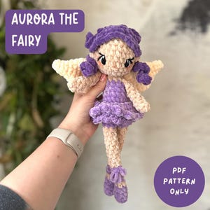 May include: A handmade crochet fairy doll named "Aurora the Fairy." The doll has a purple dress, hair, and ballet slippers, with beige wings and skin. The text "AURORA THE FAIRY" and "PDF PATTERN ONLY" are visible.