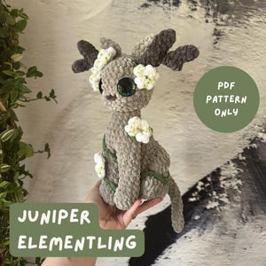 May include: A handmade crochet Juniper Elementling plushie in shades of gray, brown, and green. The plushie features large, dark eyes, decorative white flowers, and antlers. The text "PDF PATTERN ONLY" and "JUNIPER ELEMENTLING" are visible.