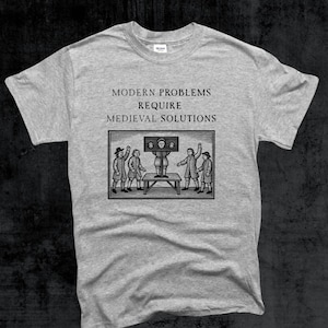May include: A light gray t-shirt with the text "MODERN PROBLEMS REQUIRE MEDIEVAL SOLUTIONS" above a black and white illustration of people around a pillory. The shirt is a Gildan brand.