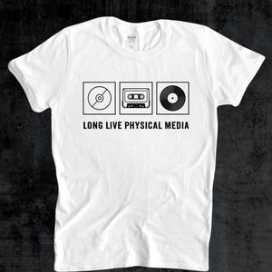 May include: White t-shirt with a black graphic of a CD, cassette tape, and vinyl record. Below the images is the text "LONG LIVE PHYSICAL MEDIA". The shirt is made of a soft material.