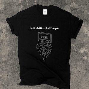 May include: Black t-shirt featuring a white graphic of a cassette tape with tangled lines and the text "lofi drift... lofi hope". The shirt is made of a soft material and has a classic crew neck.