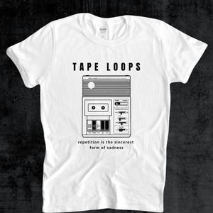 May include: White t-shirt with a black graphic of a retro cassette player and the words "TAPE LOOPS" above it. Below the cassette player is the phrase "repetition is the sincerest form of sadness."