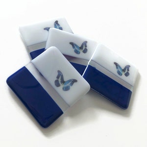 Puede incluir: Cuatro posavasos de vidrio azul y blanco con un diseño de mariposa. Cada posavasos tiene una parte superior blanca con una mariposa azul y una parte inferior azul.