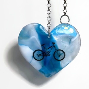 May include: A blue and white heart-shaped pendant necklace with a black mountain bike image inside. The chain is silver.